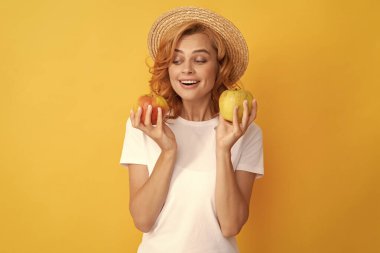 Hasır şapkalı mutlu kızıl kadın elma ve vitamin tutuyor.