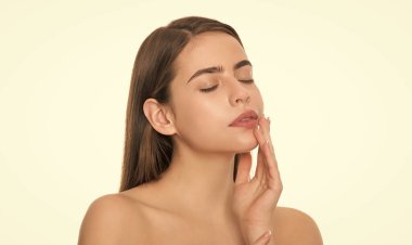 Genç bir kadın tenine dokunur, beyaz arka planda kapalı gözler, cilt bakımı
