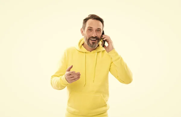 Smiling handsome mature man in hoody speaking on phone isolated on white, conversation. — Fotografia de Stock