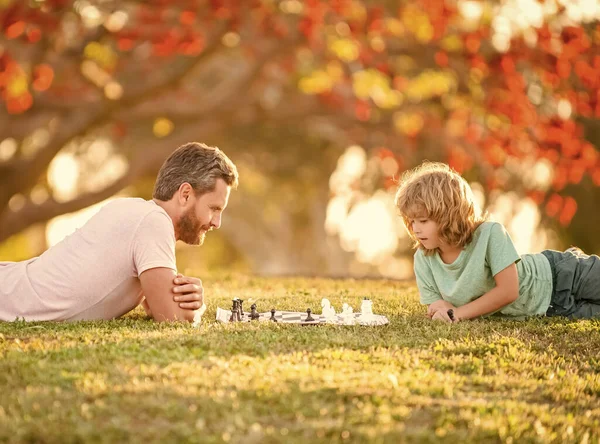 Šťastná rodina tatínek a syn dítě hrát šachy na zelené trávě v parku venku, génius — Stock fotografie