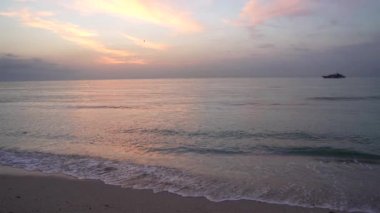 Sabah kumsalı, gün doğumunda gökyüzünde martılarla ve gemiyle, bulutlu manzarayla