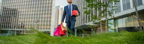 Обрезанный бизнесмен в костюме держать пакеты и подарочная коробка ходить за пределами офиса, покупки — стоковое фото