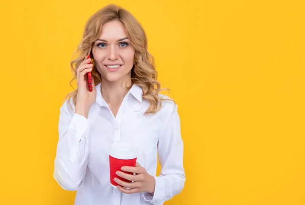 Wesoła blondynka z filiżanką kawy rozmawia przez telefon na żółtym tle — Zdjęcie stockowe