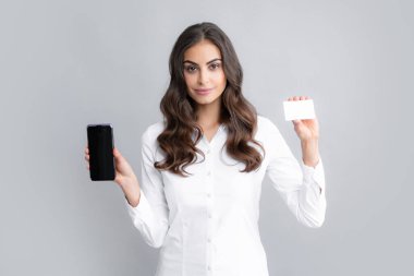 Gri arka planda izole edilmiş cep telefonu kullanan kredi kartı olan mutlu genç bir kadının portresi..