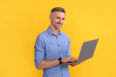 Mutlu olgun bir adam internette çalışıyor sarı arka planda bilgisayar, iş