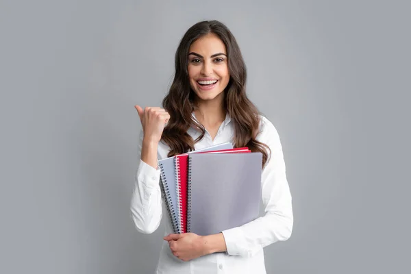 Gelukkige lachende student of leraar. Tiener meisje met notitieboekjes staan over grijze achtergrond met kopieerruimte. Educatief concept voor school. Portret van een jonge student. Winnaars bord. — Stockfoto