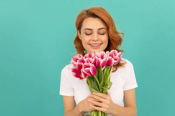 Mavi arka planda lale çiçeği kokusu alan mutlu bir kadın. — Stok fotoğraf