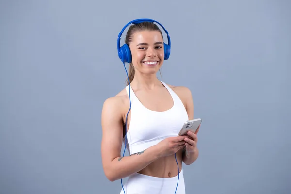헤드폰을 가진 뚱뚱 한 소녀는 스포츠를 위해 음악을 선택 한다. 스포츠 의상을 입고 웃고 있는 행복 한 젊은 여자. 근육 건강 모델. — 스톡 사진