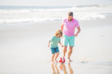 Aile tatilleri. Spor aktivitesi. Baba ve oğul plajda futbol oynuyorlar. Baba ve çocuk çocuk.