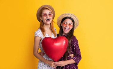 Sarı arka planda aşk balonu tutan anne ve kız hayrete düştü.