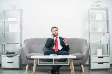 İş adamı ofisinde oturuyor ve telefonda konuşuyor.