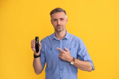 Gri saçlı adam elektrikli jilet sunuyor. Saç bakımı ve tıraş. Kişisel bakım ve cilt bakımı.