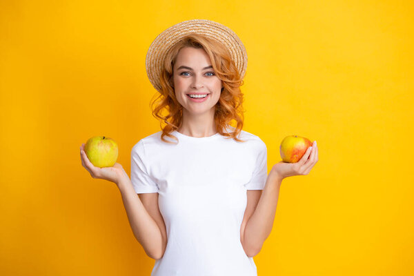 Smiling redhead woman in summer straw hat with healthy teeth holding apple. studio isolated portrait.