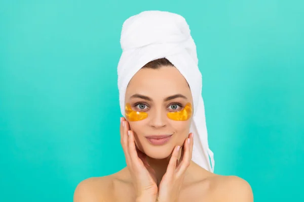 Sorridente giovane ragazza ha macchie di collagene occhi dorati sul viso con asciugamano — Foto Stock
