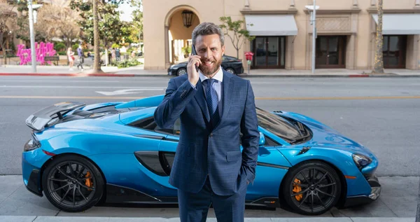 handsome businessman talk on phone next to luxury car