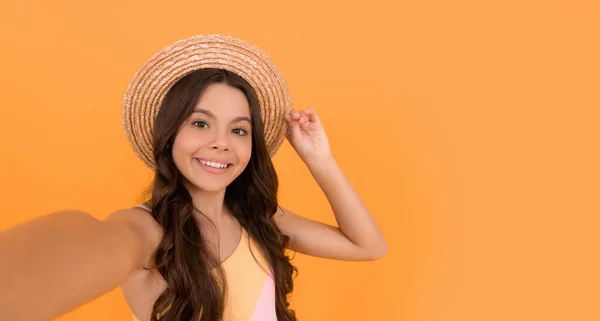 Счастливая девочка-подросток в летней соломенной шляпе делает селфи на оранжевом фоне, копирует пространство, делает селфи — стоковое фото