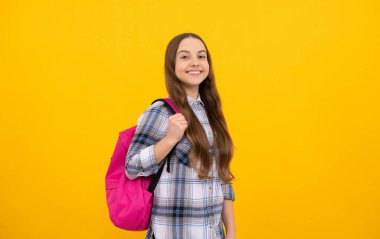 Sarı arka planda okul çantası olan kareli tişörtlü mutlu çocuk, okul.
