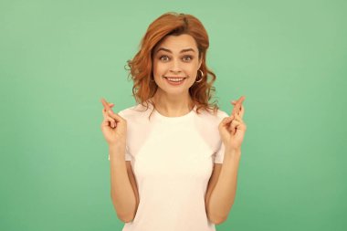 Kıvırcık saçlı mutlu kadın mavi arka planda bir dilek diliyor.