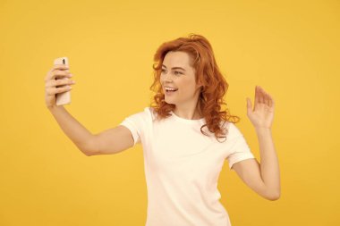 Heyecanlı, mutlu genç bir kadının görüntüsü, sarı arka planda izole edilmiş, kamerayla selfie çekiliyor..