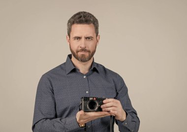 Sıradan tişörtlü sakallı adam. Elinde aralık bulucu fotoğraf makinesi, elinde gri arka plan, fotoğrafçılık.