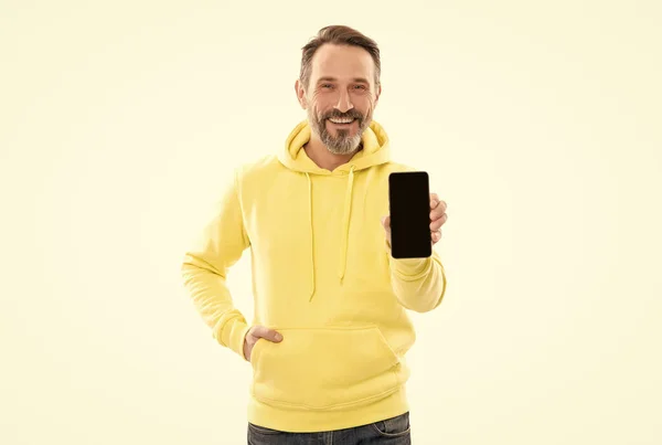 Kapüşonlu mutlu olgun bir adam akıllı telefon ekranı sunar. Kopya alanı beyaza izole edilir, terfi ettirilir.. — Stok fotoğraf