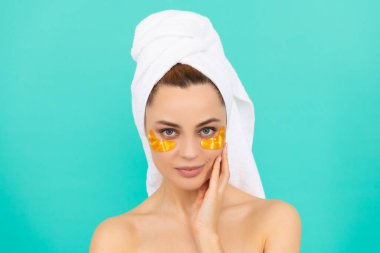 Genç kızın yüzünde havluyla kolajen altın göz bantları var.