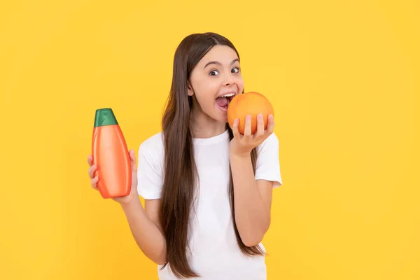 Šťastný dítě držet šampón láhev a jíst grapefruit na žlutém pozadí, vitamin — Stock fotografie