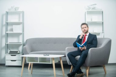 Takım elbiseli olgun bir adam ofiste planlamacıyla oturuyor.