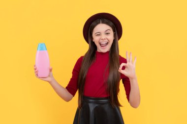 Şapkalı neşeli çocuk saç kremi şişesini tutuyor. Sarı arka planda jest, duş jeli.