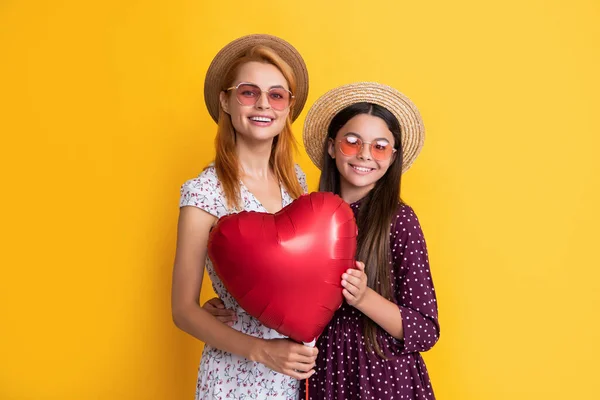 Улыбающиеся мать и дочь держат воздушный шар любви на желтом фоне — стоковое фото