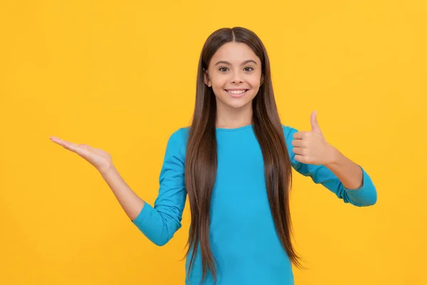 Gelukkig kind met duim omhoog presenteren product op gele achtergrond met kopieerruimte, reclame — Stockfoto