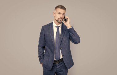 Gri saçlı, resmi takım elbiseli olgun bir adam telefonda konuşuyor, pazarlık yapıyor.