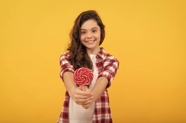 Uzun kıvırcık saçlı mutlu çocuk sarı arka planda lolipop karamel şekeri ve diş bakımı gösteriyor..