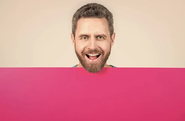 Счастливый взрослый бородатый мужчина за бланшированным розовым бумажным баннером с копировальным местом для информации, продажи — стоковое фото