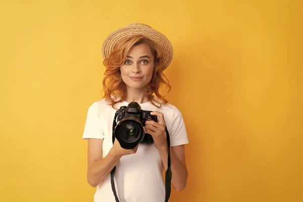 Uśmiechnięta ruda kobieta fotograf z aparatem fotograficznym w słomkowym kapeluszu podejmowania zdjęć, fotografia — Zdjęcie stockowe