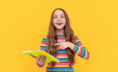 Mutlu çocuk gülümsüyor okul kitabı sarı arka planını işaret ediyor, çalışıyor.