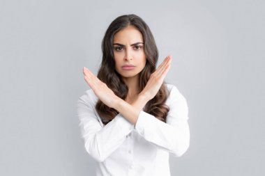 Negatif kadın ellerini çapraz yapmış. Gri arka planda izole edilmiş yasak bir kural yok. Memnun olmayan kızgın kadın teklifi engelliyor, çapraz duruş hareketi gösteriyor, olumsuz yanıt.