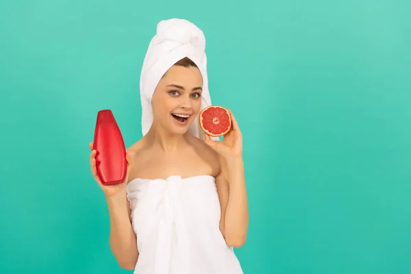 Surprised lady in towel with grapefruit shampoo bottle on blue background — Stock Photo, Image
