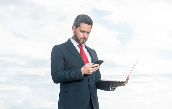 businessman in suit checking smartphone and hold laptop