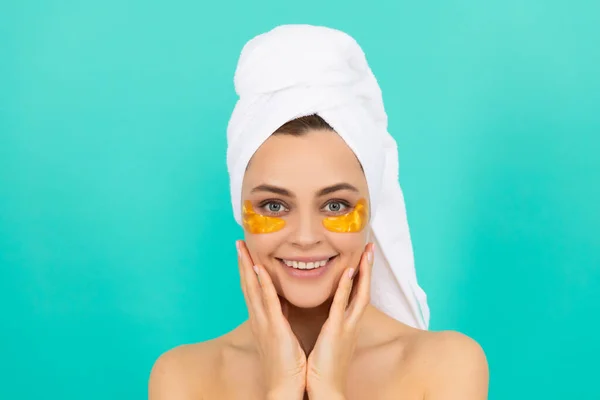 У веселой юной леди золотые коллагеновые повязки на лице с полотенцем — стоковое фото