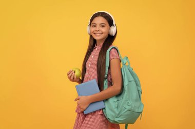 Kulaklıklı mutlu okul çocuğu öğle yemeği için sırt çantası ve çalışma kitabı taşıyor, sağlıklı bir yaşam tarzı..