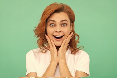 Şaşırmış kızıl saçlı, kıvırcık saçlı ve sağlıklı tenli, mavi arka planda, sürpriz..