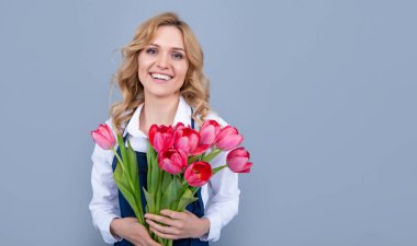 Gri arka planda bahar lale çiçekleri olan önlüklü mutlu çiçek satıcısı kadın..