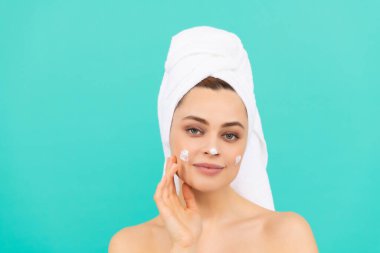 Neşeli genç kız mavi arka plana yüz kremi sür..