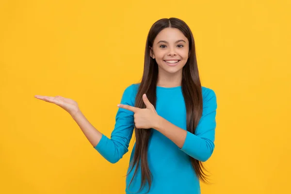 髪の長い幸せな子供が製品を提示し コピースペース 広告と黄色の背景に指を指す — ストック写真