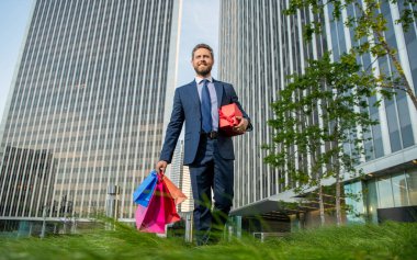 Takım elbiseli neşeli, olgun iş adamı hediye paketleri ve hediye kutusunu ofisin dışında tutuyor..