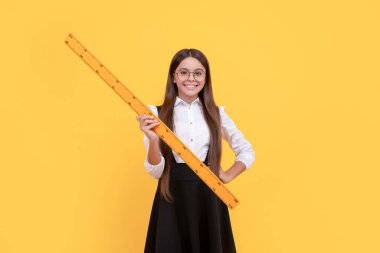 Okul üniformalı ve gözlüklü neşeli çocuk ölçüm ve geometri için matematik cetveli tutuyor.