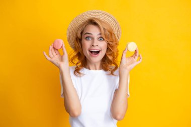 Tatlı, genç bir kadın. Kurabiye tutuyor. Güzel gülümseyen genç kız sarı arka planda renkli badem kurabiyeleri yiyor.