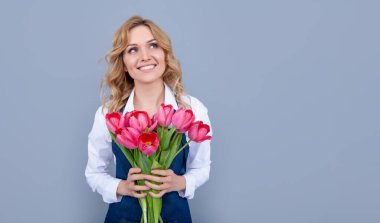 Gri arka planda bahar lale çiçekleri olan önlüklü mutlu çiçek satıcısı kadın..