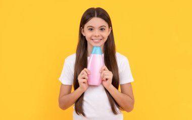 Mutlu çocuk sarı arka planda şampuan şişesi tutuyor, kozmetik..